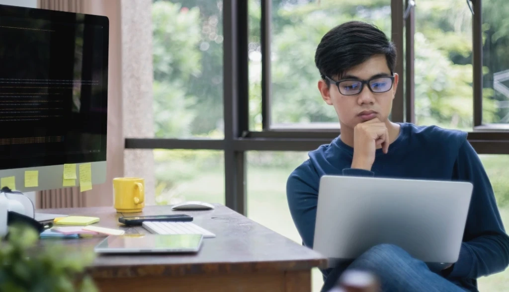 Jovem rapaz está sentado, em frente ao computador, a trabalhar no currículo para o primeiro emprego.